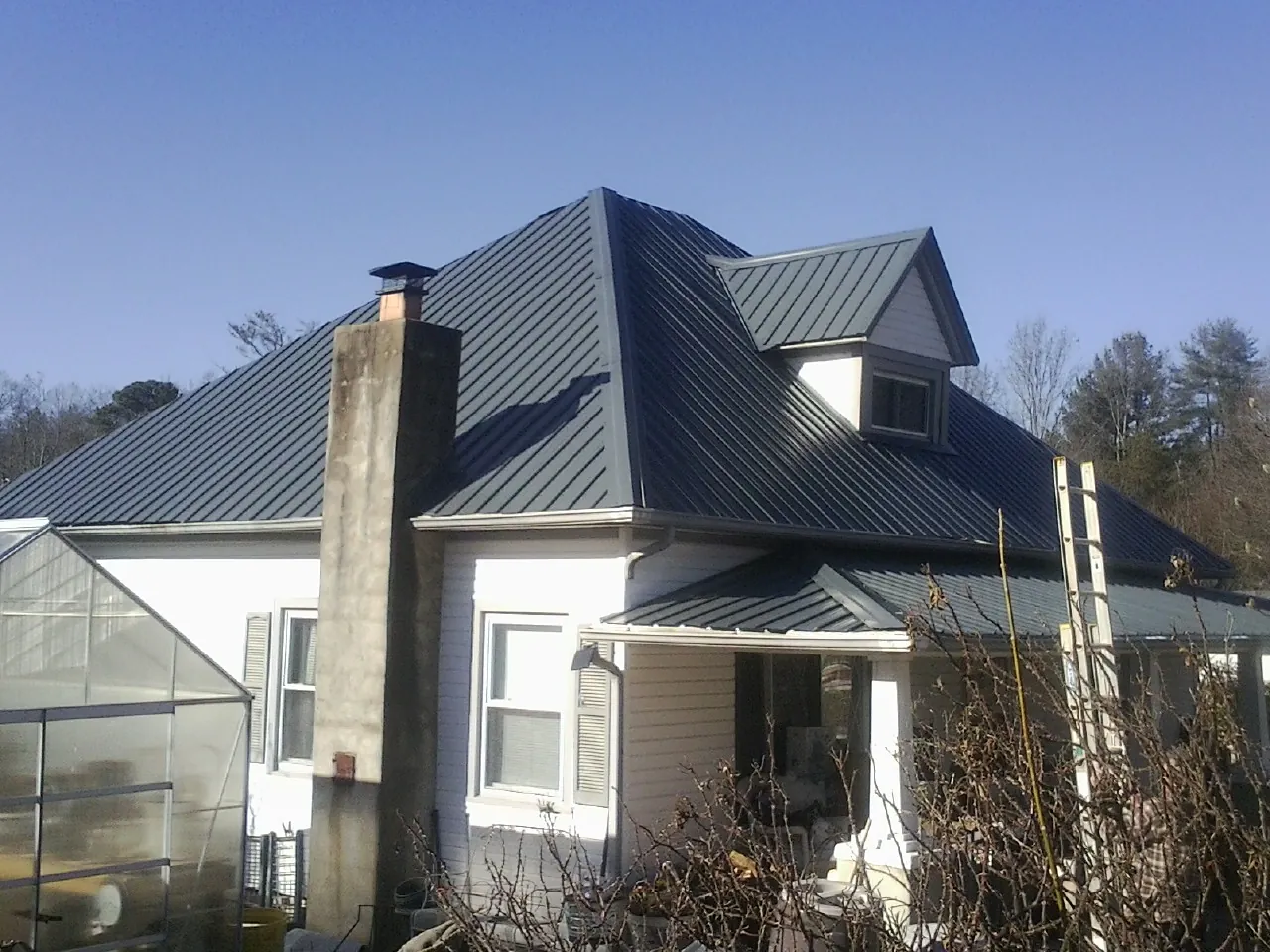 Dark blue standing seam metal roof on a white farmhouse with dormer in Durkee