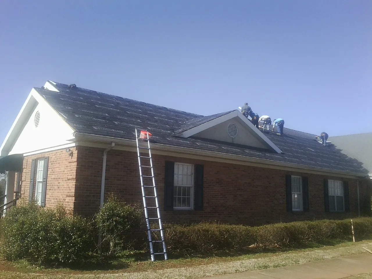 Crew tearing shingles off a brick ranch roof with a ladder set — Emergency Roof Repair work by our crew in Durkee