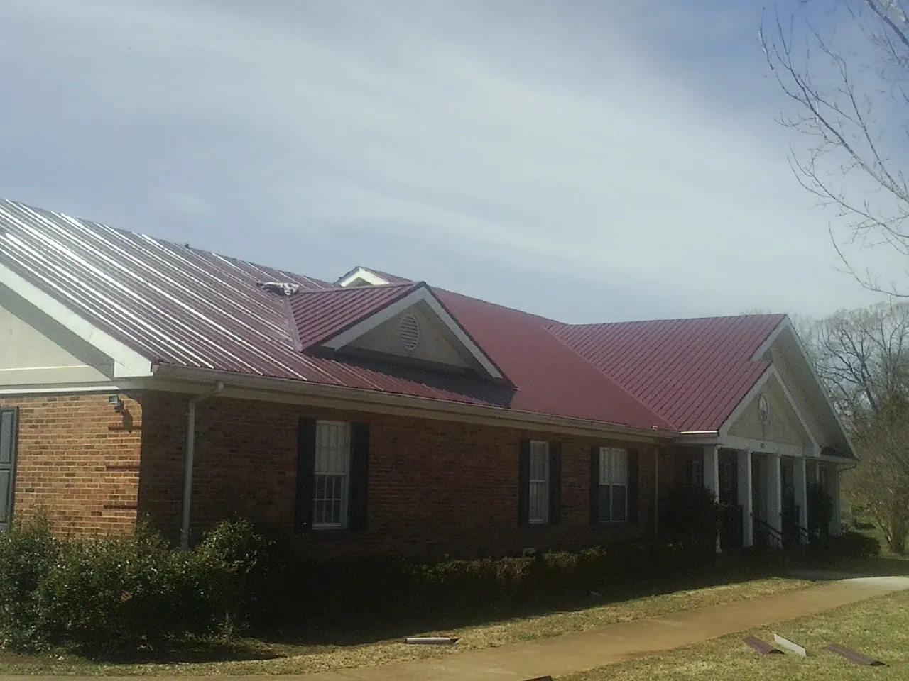 Red metal roof with gabled entries on a long brick building, from a Hail Damage Roof Repair job in Durkee