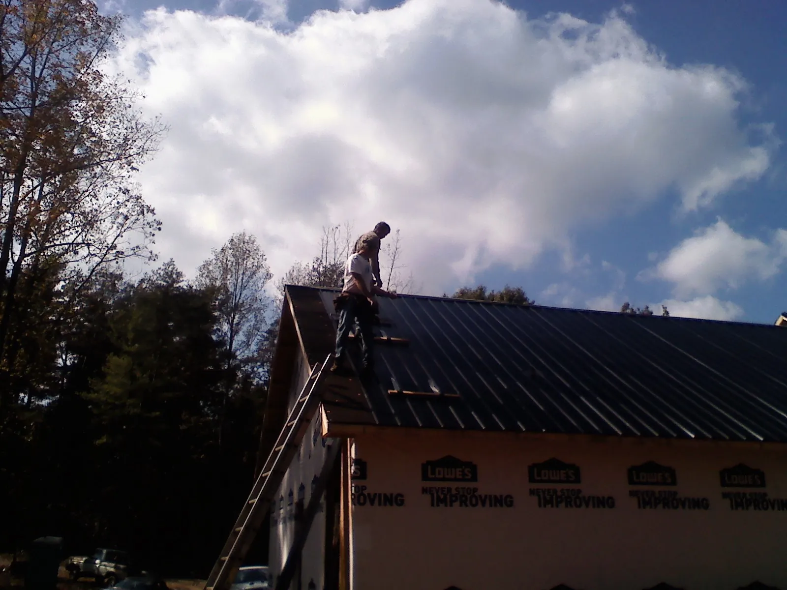 Roofer fastening dark metal panels high against a cloudy sky, from a Roof Inspection job in Durkee